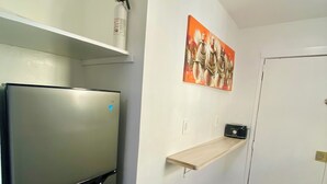 Una cocina compacta con un refrigerador de acero inoxidable, un estante de madera, una radio montada en la pared y una puerta con manija.