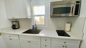 Una cocina con armarios blancos, un microondas de acero inoxidable, una cafetera y una ventana.