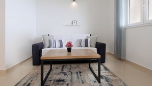 Una sala de estar moderna con un sofá, una mesa de centro, un tapiz, un estante en la pared y un ventanal con cortinas.