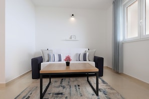 Ein modernes Wohnzimmer mit einer Couch, einem Couchtisch, einem Teppich, einer Wandregal und einem Fenster mit Vorhängen.