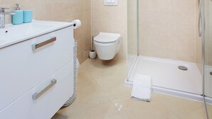 Un baño moderno con ducha de vidrio, un lavamanos blanco con espejo y un inodoro.
