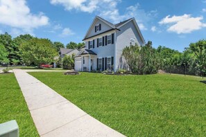 Une maison à deux étages avec un jardin devant, une allée et une clôture.