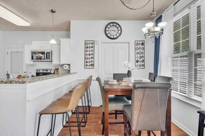 A modern kitchen with a microwave, stove, and dining area with chairs and a table. - King Bed - Hot Tub - Fenced Yard - Near Carowinds (Charlotte)
