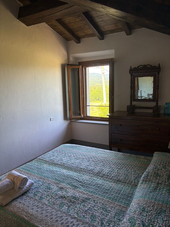 A bedroom with a bed, a dresser, a mirror, and a window with a view of greenery.