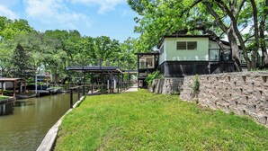 A riverside property with a dock, a stone wall, and a house with multiple levels. - Riverview Hideaway: Waterfront & Boat Lift! (Kingsland)