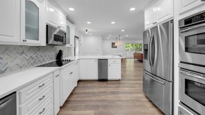 A modern kitchen with white cabinetry, stainless steel appliances, and a herringbone-patterned backsplash. - Riverview Hideaway: Waterfront & Boat Lift! (Kingsland)