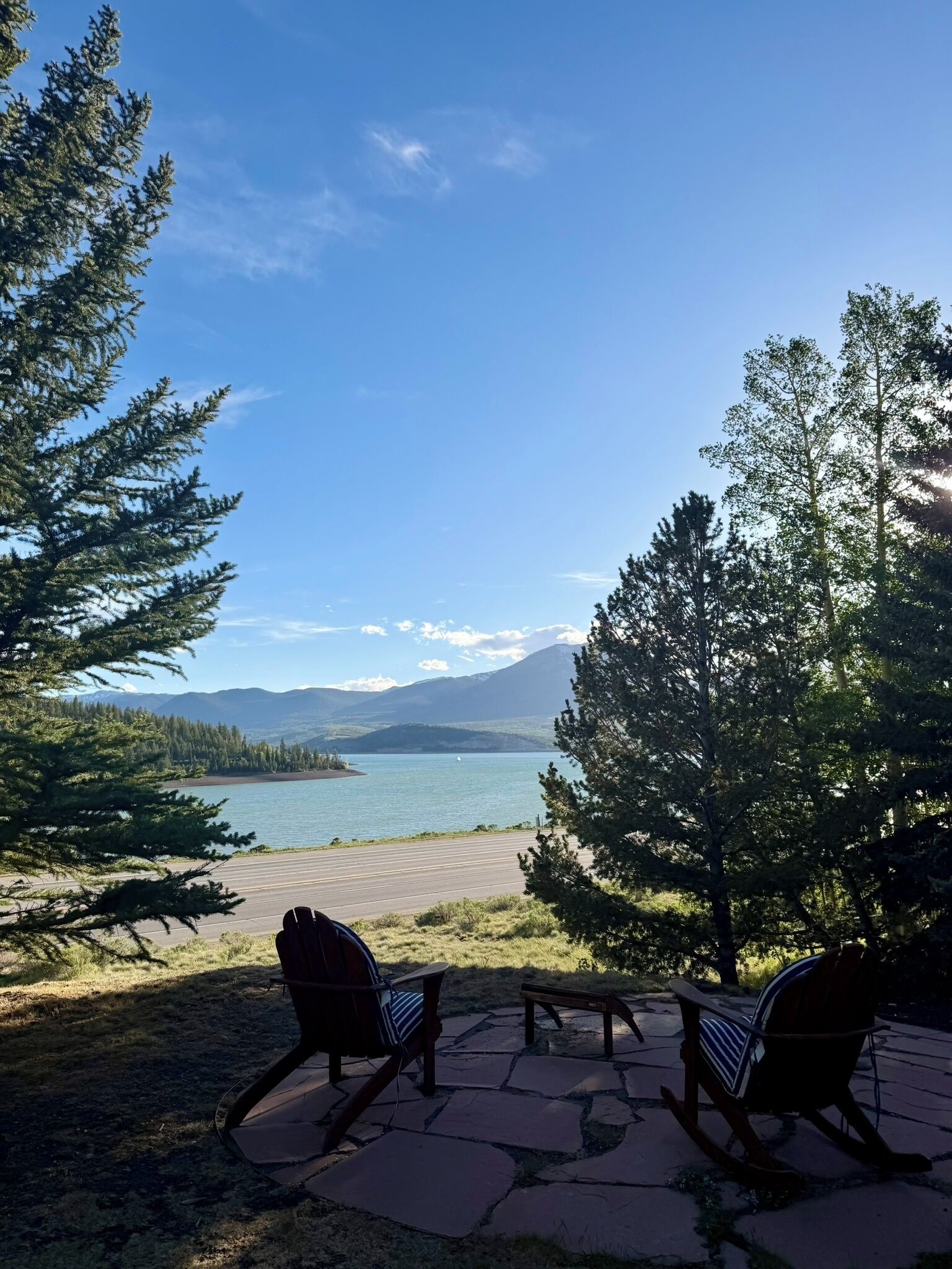 A patio with two rocking chairs overlooking a lake, surrounded by trees and mountains.