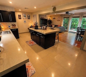 A modern kitchen with a central island, a dining area with a table and chairs, and a living space with a sofa and TV. - Pool Home-World Cup-10 Min AT&T Stadium-Sleeps 10 (Grand Prairie)