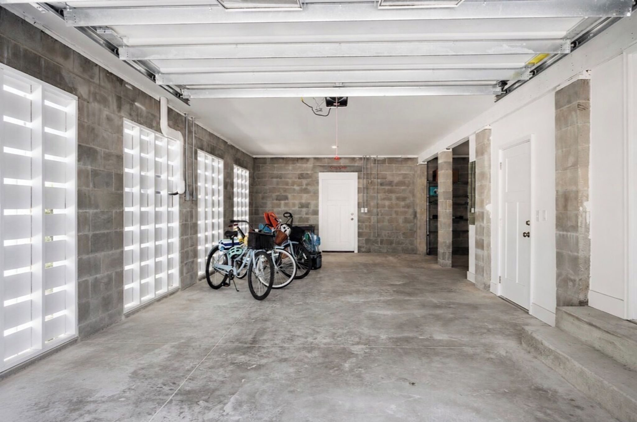 Un garaje espacioso con pisos y paredes de concreto, que muestra varias bicicletas y una puerta blanca.