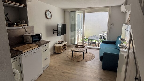 A modern apartment with a kitchen, dining area, and living room, featuring a large sliding glass door to a balcony.