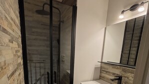 A modern bathroom with a glass-enclosed shower, a white sink, and a mirror above it.