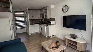 A modern apartment with a kitchenette, a living area with a sofa, a coffee table, and a TV.