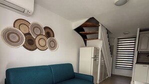 A living room with a teal sofa, a small kitchen with a refrigerator, and a staircase leading to an upper level.