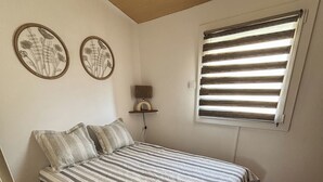 A bedroom with a bed, wooden flooring, a window with blinds, and two wall-mounted floral decorations.