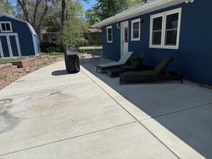 A covered patio area with a grill, two lounge chairs, and a small table. - Lovely 3-bedroom house in Colorado Springs. Close to MANY attractions! (Colorado Springs)
