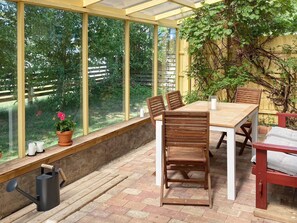 Ein Wintergarten mit Holztisch und Stühlen, einer Topfpflanze und einem Gießkanne.