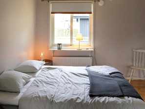 Ein Schlafzimmer mit einem Bett, einem Nachttisch, einer Lampe und einem Fenster.