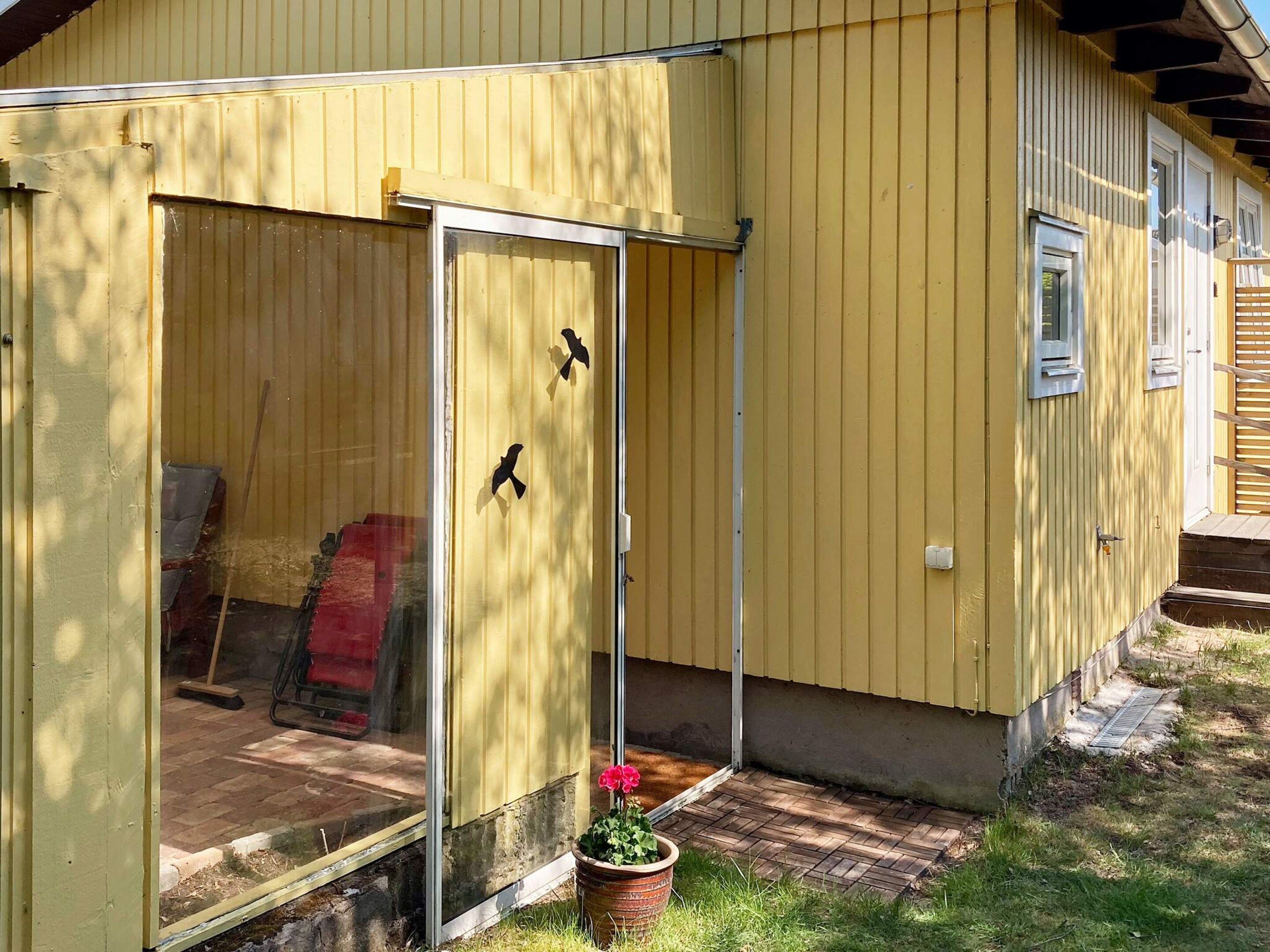 En gul bygning med skydedør, en lille veranda og en potteplante.