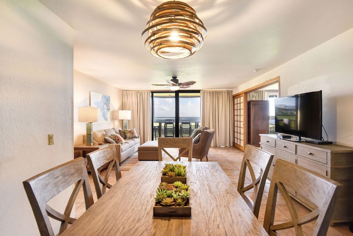 Habitación de hotel con mesa de comedor, sillas, televisión, sofá, lámpara y vistas al exterior.