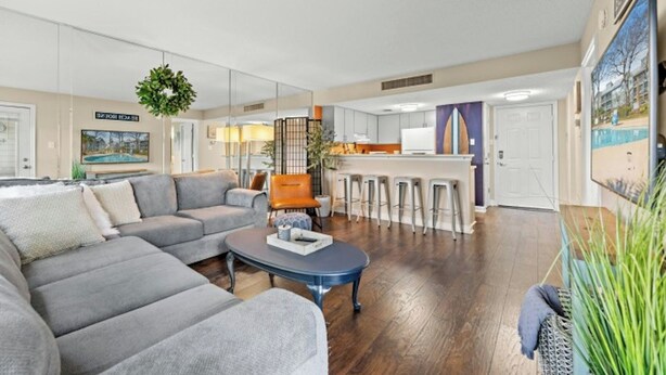 A living room with a grey sofa, a coffee table, and a kitchen area with bar stools. - MB Five Seasons 6203- 1BR Close to Beach (Myrtle Beach)