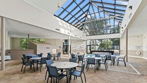 An indoor patio area with tables and chairs, a glass ceiling, and a brick floor. - MB Five Seasons 6203- 1BR Close to Beach (Myrtle Beach)