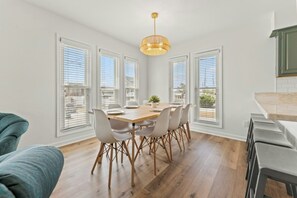 A dining area with a wooden table and chairs, large windows with blinds, and a hanging light fixture. - Endless Summer - Cherry Grove - 1 Block from Beach (North Myrtle Beach)