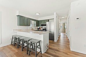 A modern kitchen with green cabinets, a white island with bar stools, and a stainless steel refrigerator. - Endless Summer - Cherry Grove - 1 Block from Beach (North Myrtle Beach)