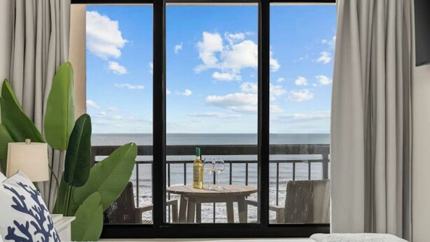 Ein Hotelzimmer mit großem Fenster, einem Bett, einem Tisch mit Flasche und Gläsern sowie einer Zimmerpflanze.