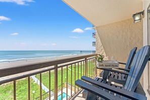 Ein Balkon mit Blick auf Strand und Meer, ein Schild mit der Aufschrift 'hello Sweet Cheeks' und ein kleiner Tisch mit zwei Gläsern.