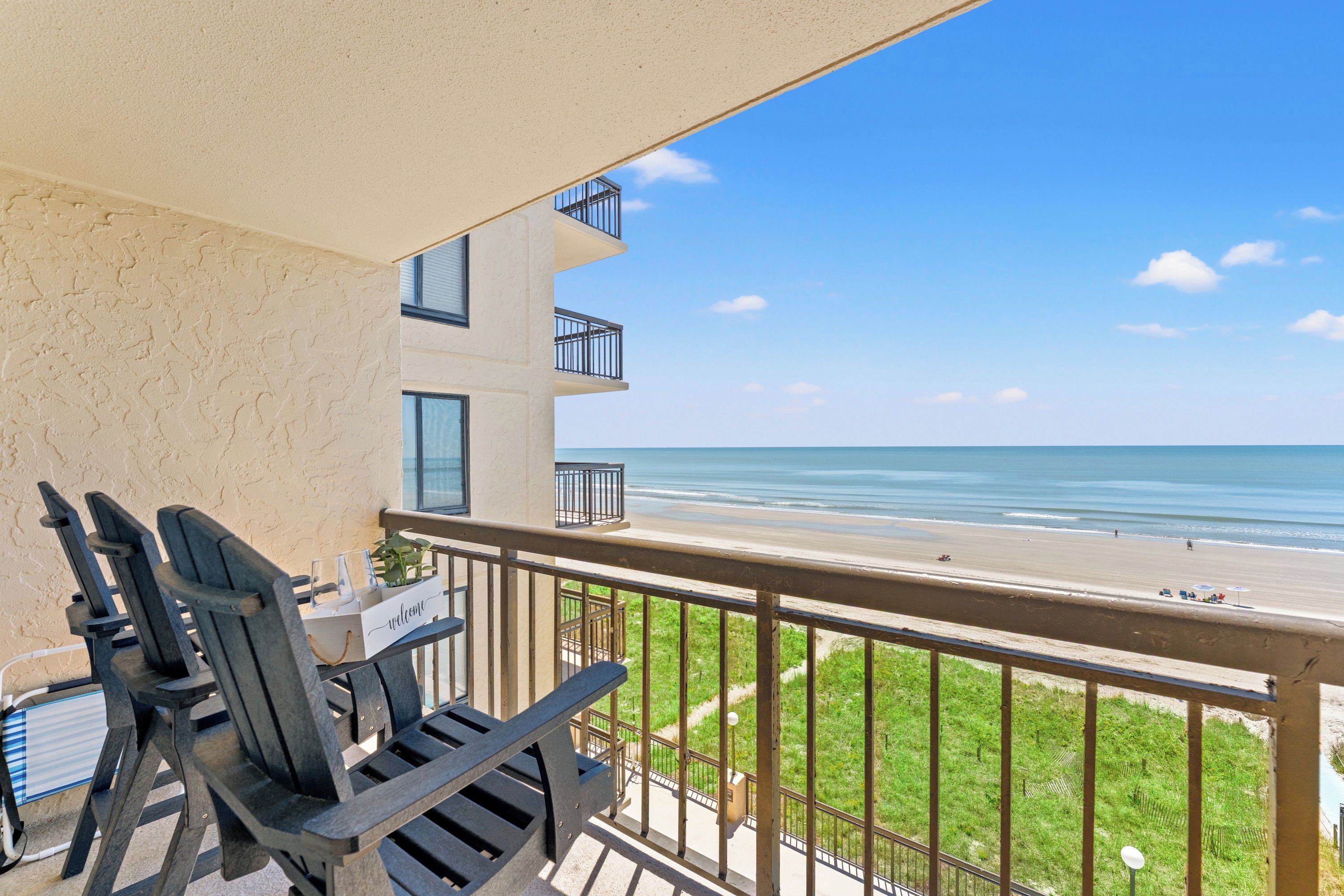 Un balcon avec vue sur la plage, une pancarte de bienvenue et du mobilier d’extérieur.