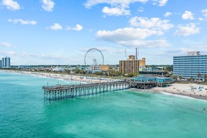Eine Küstenstadt mit einer Mole, die sich in türkisfarbenes Wasser erstreckt, einem großen Riesenrad und einem Hotel am Strand.