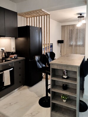 Een moderne keuken met een zwarte koelkast, een houten scheidingswand, een eettafel met stoelen en een klein plankje met decoratieve objecten.