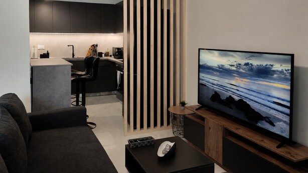 Ein modernes Wohnzimmer mit einer Couch, einem Couchtisch, einem Fernseher und einer Küchenzeile im Hintergrund.