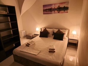 Een slaapkamer met een bed, twee nachtkastjes, een wandplank en een schilderij.