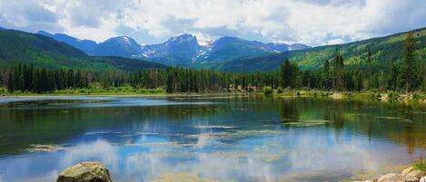 A mountain landscape with a lake, clear skies, and a large rock in the foreground.