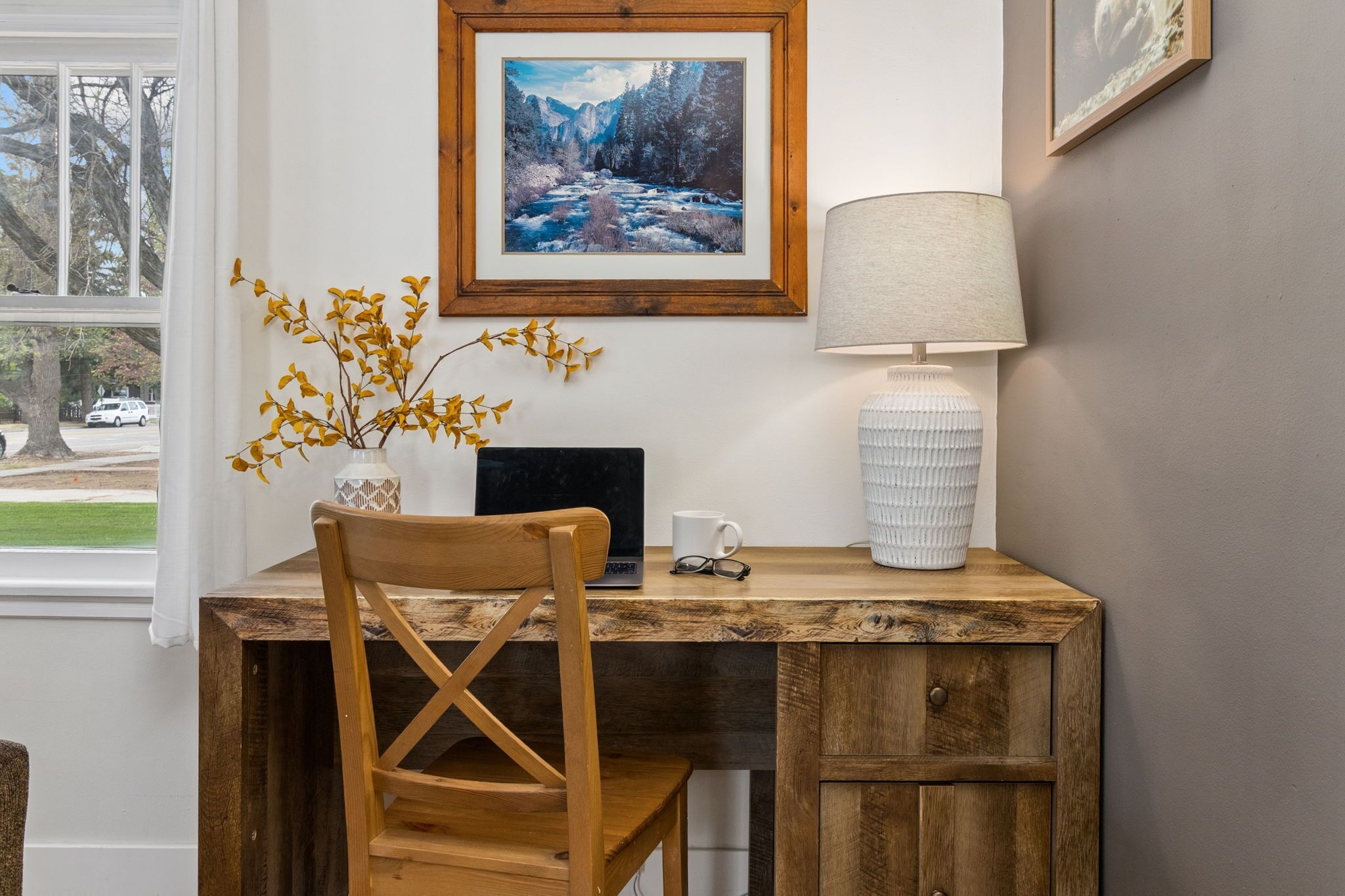 A wooden desk with a laptop, a lamp, and a vase with dried flowers.