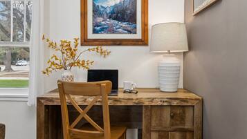 A wooden desk with a laptop, a lamp, and a vase with dried flowers.