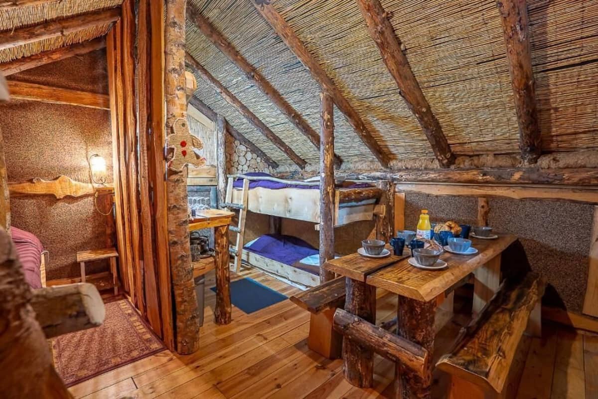 Ein rustikaler Raum mit Holztisch, Stockbetten und einem Strohdach.