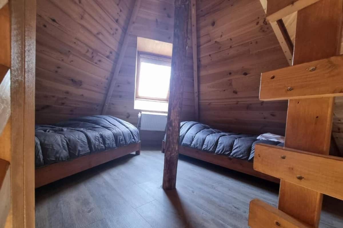 Ein Loft-Zimmer mit zwei hölzernen Etagenbetten, einer geneigten Decke und einem Fenster, das für natürliches Licht sorgt.