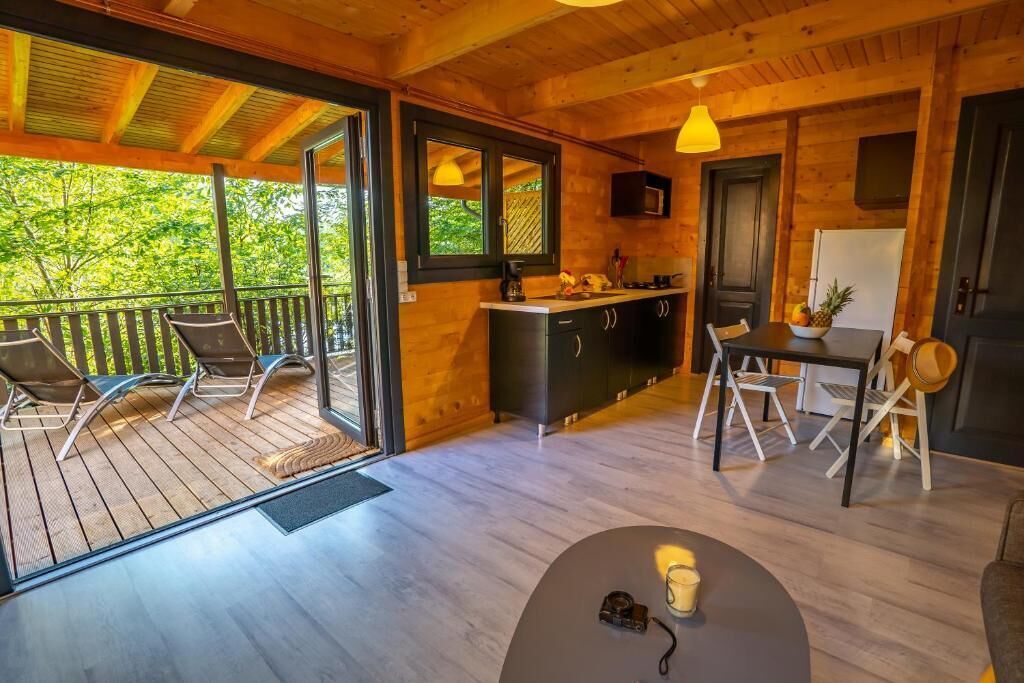 A wooden cabin with a balcony, a kitchen area, and a dining table with chairs.
