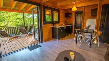A wooden cabin with a balcony, a kitchen area, and a dining table with chairs.