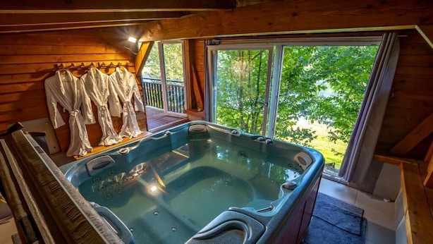 A hot tub in a wooden cabin with a view of trees.