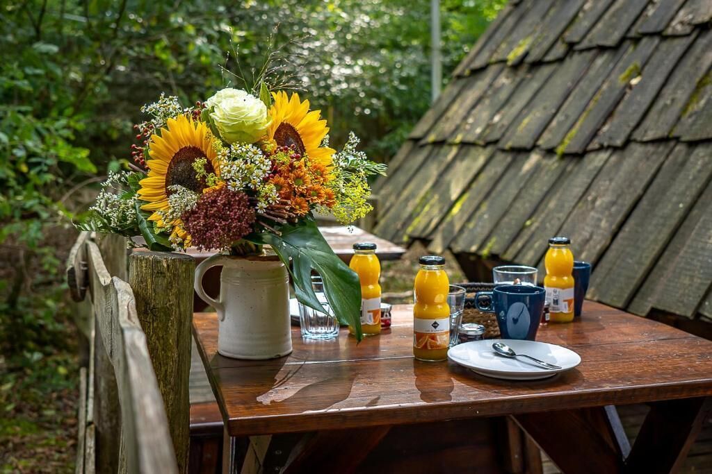 Een rustieke houten tafel met een bloemstuk, een karaf en diverse drankflessen en glazen.