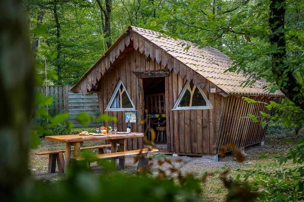 Une cabane en bois rustique, dotée d’un toit à deux versants, d’une porte en bois et d’une table de pique-nique devant l’entrée.