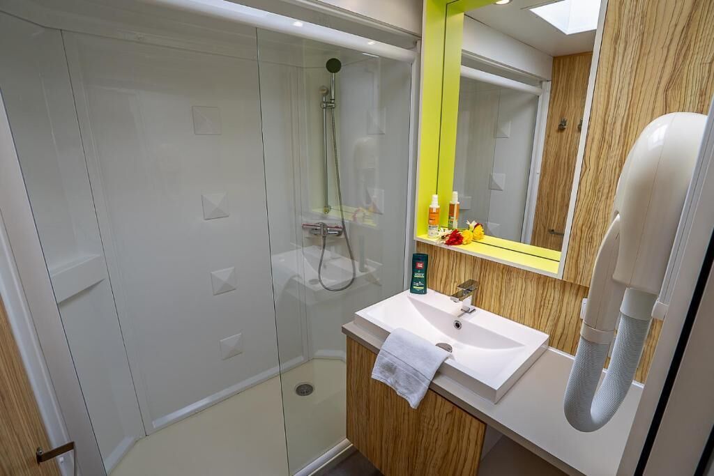 Une salle de bain moderne avec une douche à parois de verre, un lavabo blanc et un miroir avec un cadre jaune.
