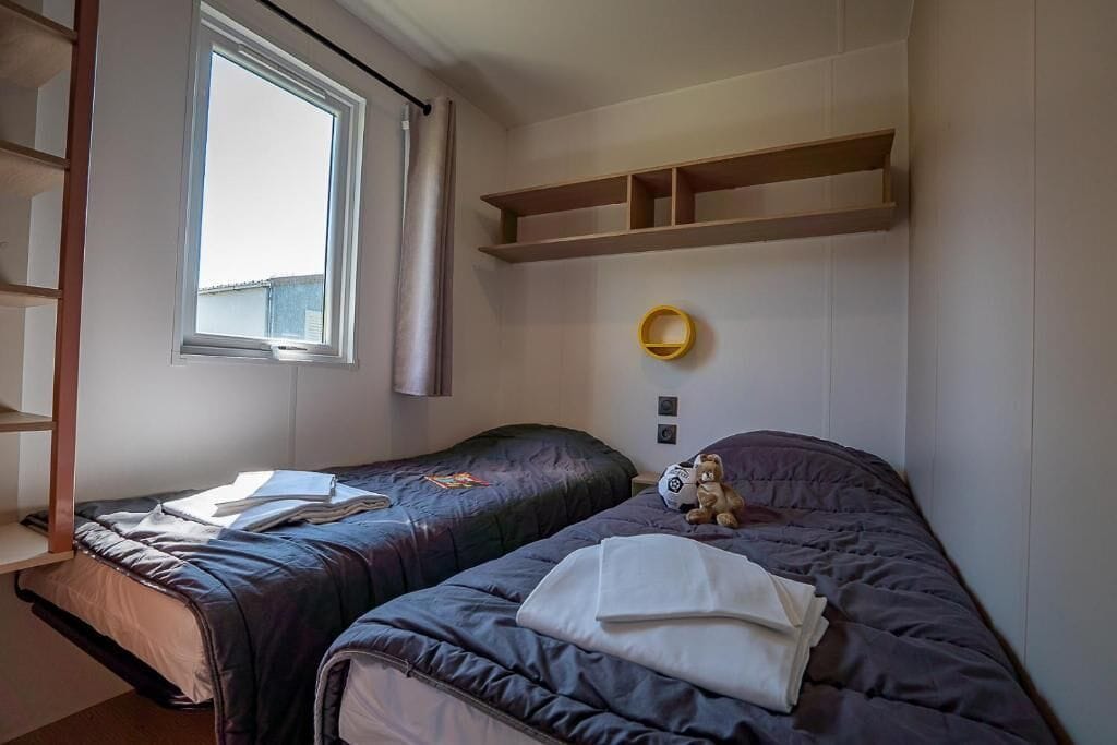 Un dormitorio con dos camas, una ventana, una estantería y una lámpara de pared.