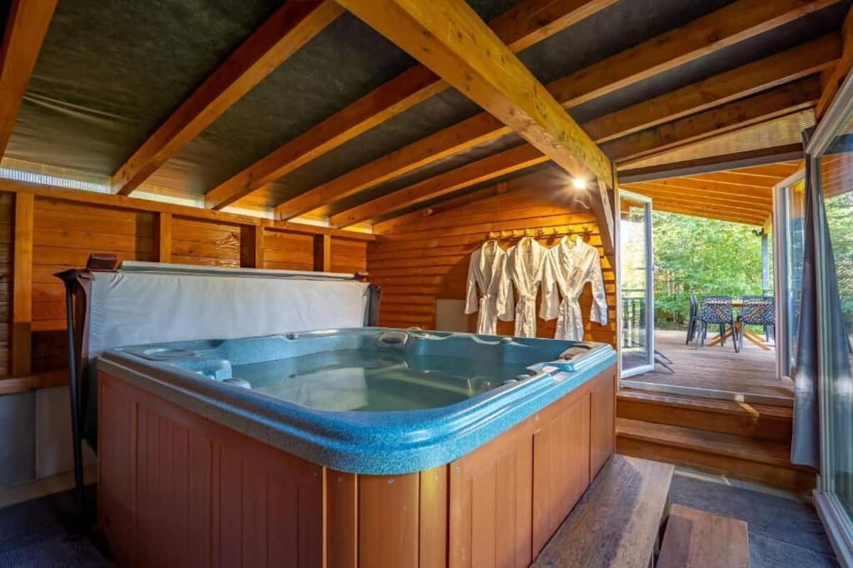 Eine Holzhütte mit Whirlpool, Holzwänden und einer Terrasse mit Sitzgelegenheit.