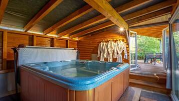 Een houten chalet met een hottub, houten wanden en een terras met zitplaatsen buiten.