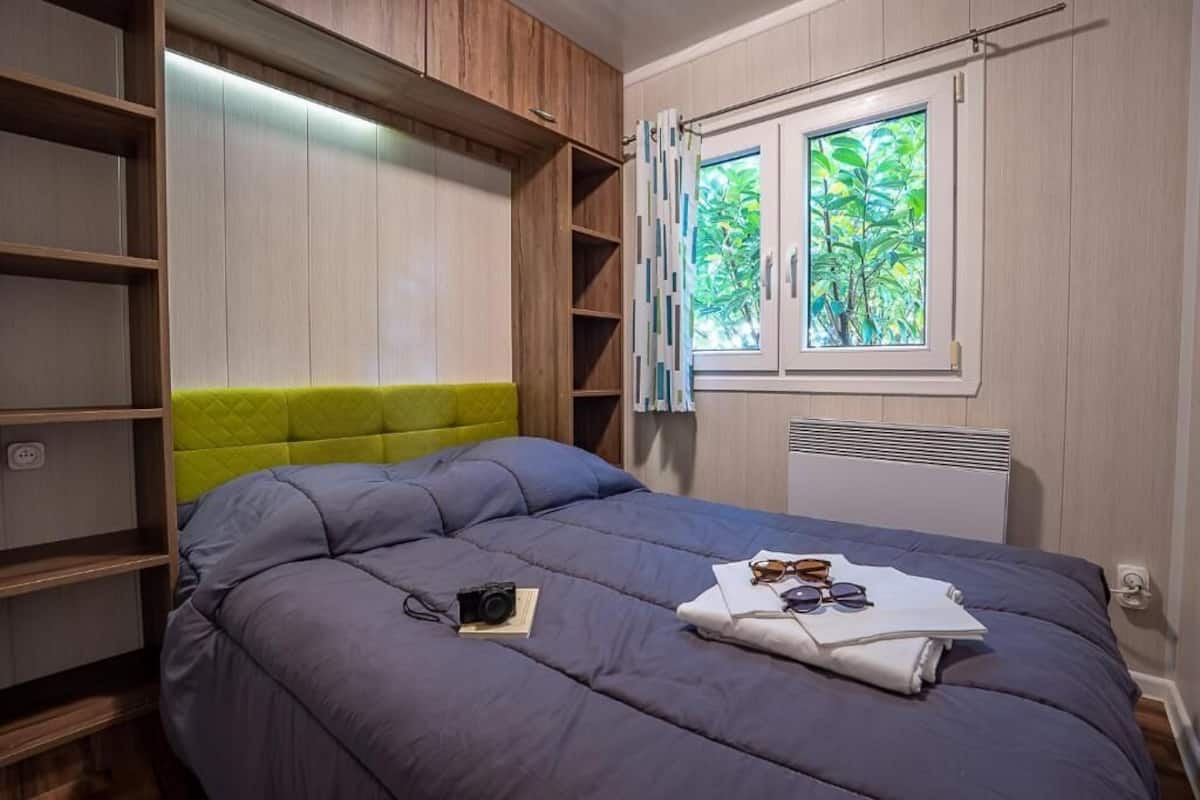Ein Schlafzimmer mit Bett, Kleiderschrank, Fenster und Blick ins Grüne sowie einer Heizung.