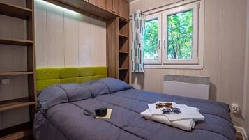 Un dormitorio con cama, armario, ventana con vistas a zonas verdes y radiador.